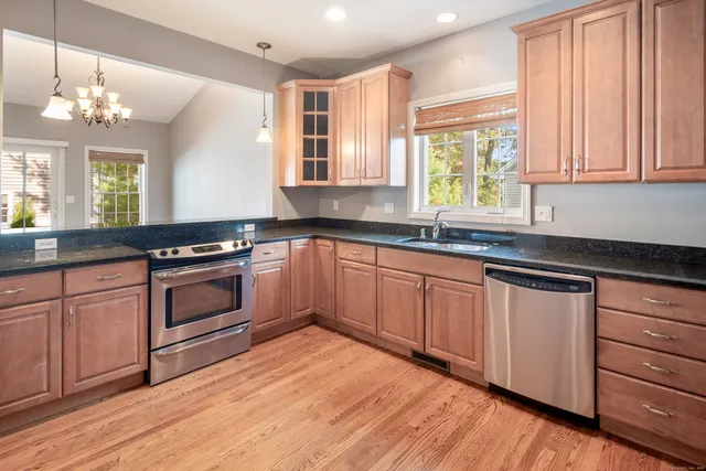a kitchen with granite countertop a stove a sink and dishwasher wooden cabinets with wooden floor