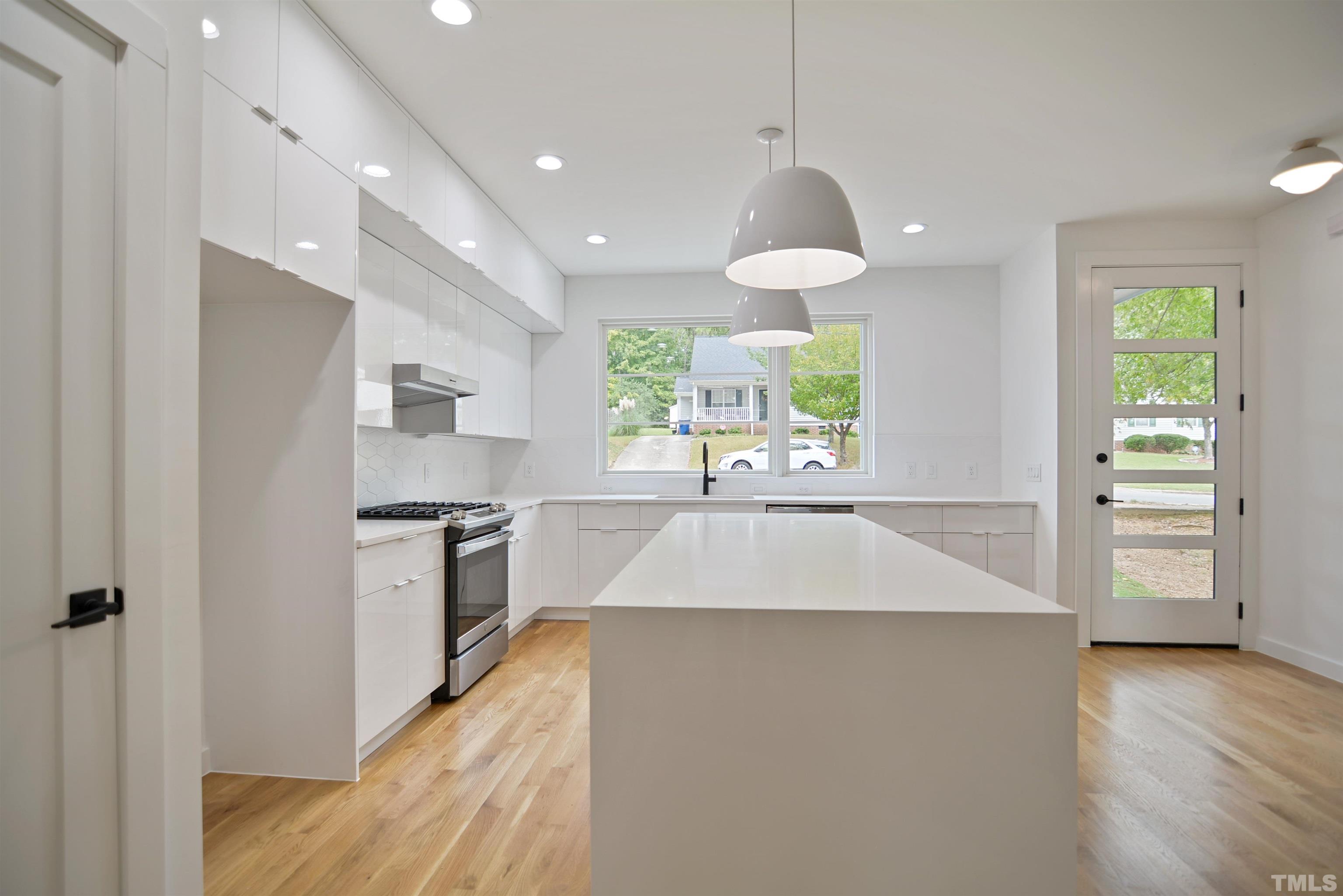 1306 East Lenoir Street Raleigh, NC 27610 - Photo 10 of 26 a large kitchen with stainless steel appliances a large counter top a stove a chimney a sink and a large window