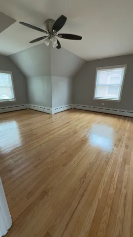 an empty room with wooden floor fan and windows