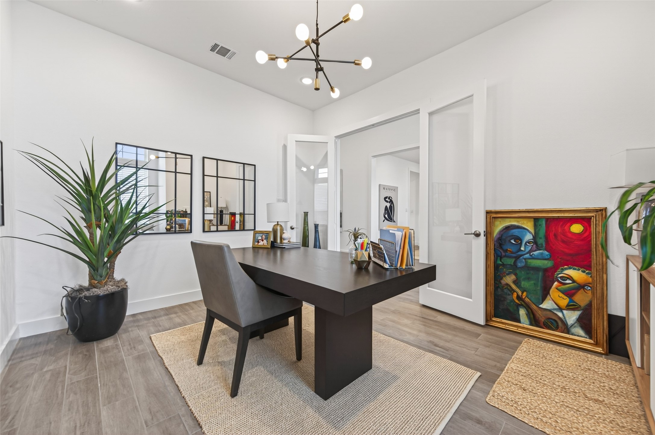 29612 Fulshear Lake Trace Fulshear, TX 77406 - Photo 13 of 48 This photo showcases a modern home office with a sleek black desk, stylish lighting, and contemporary artwork. The room features wood flooring, a large plant, and glass doors, creating a bright and inviting workspace.