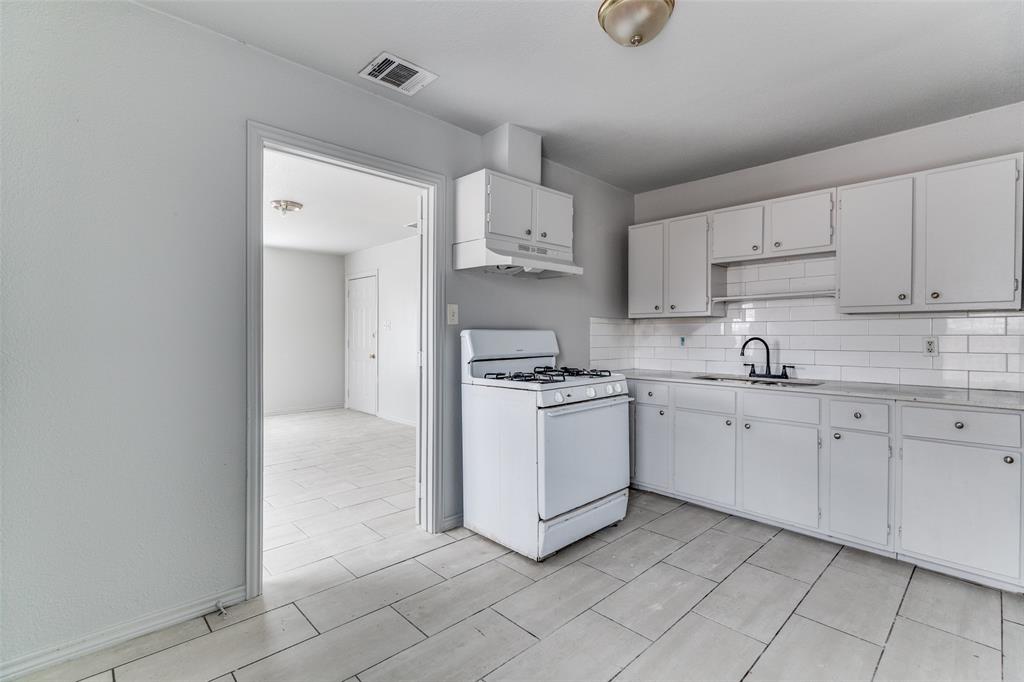 7909 Wanebe Drive Dallas, TX 75235 - Photo 20 of 25 Kitchen with white gas stove, light countertops, decorative backsplash, and white cabinets
