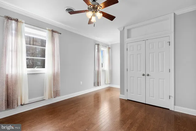 an empty room with wooden floor chandelier fan and windows