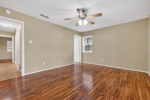 a view of an empty room with wooden floor and a ceiling fan