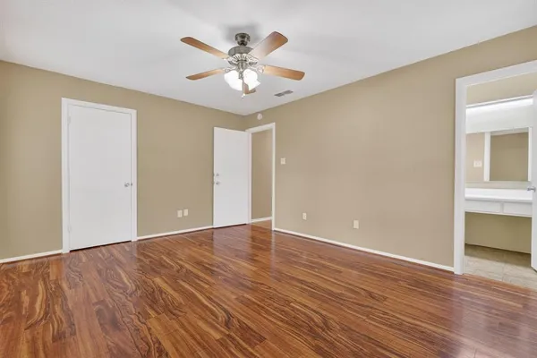 a view of an empty room with wooden floor and a ceiling fan