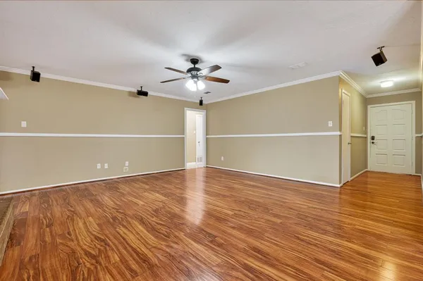 a view of an empty room with wooden floor and a ceiling fan