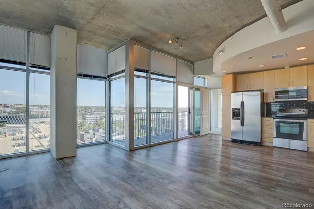 a view of an empty room with wooden floor and a kitchen