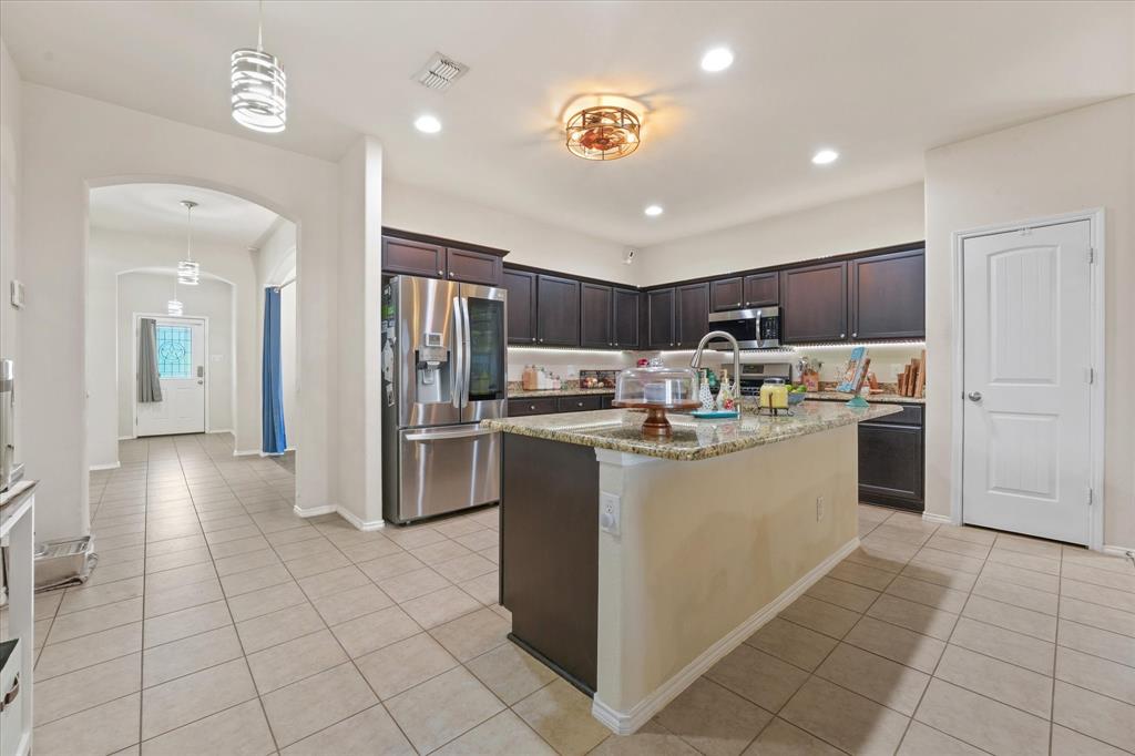 3801 Surf Street Denton, TX 76208 - Photo 7 of 29 Kitchen with arched walkways, dark wood finish cabinetry, stainless steel appliances, light stone countertops, and a kitchen island with sink