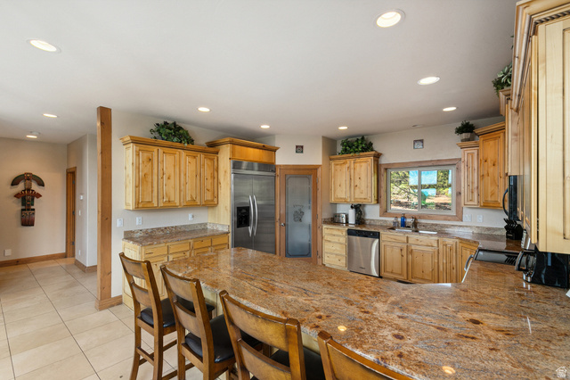 755 South Zion Ridge Drive Orderville, UT 84758 - Photo 42 of 84 Kitchen featuring a peninsula, black appliances, a breakfast bar, light stone counters, and light wood finish cabinetry