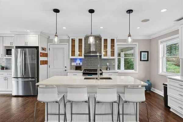 a kitchen with stainless steel appliances kitchen island granite countertop a dining table chairs and white cabinets