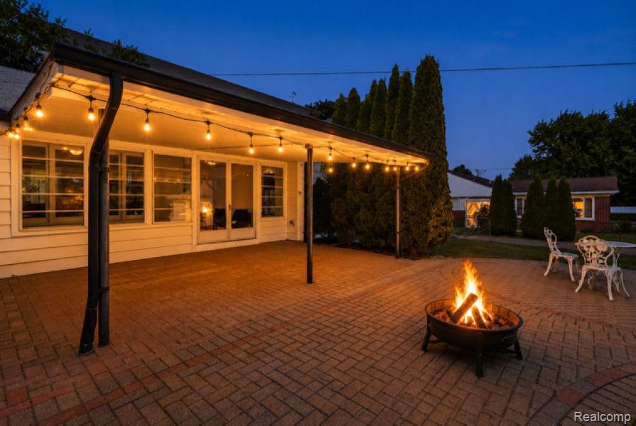 8710 32 Mile Road Washington, MI 48095 - Photo 48 of 60 Paved patio area featuring a covered porch with string lighting, a circular fire pit, and mature perimeter landscaping