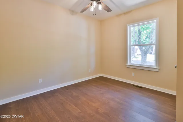 a view of an empty room with wooden floor and window