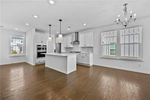 a large kitchen with kitchen island a stove a sink a refrigerator and white cabinets with wooden floor