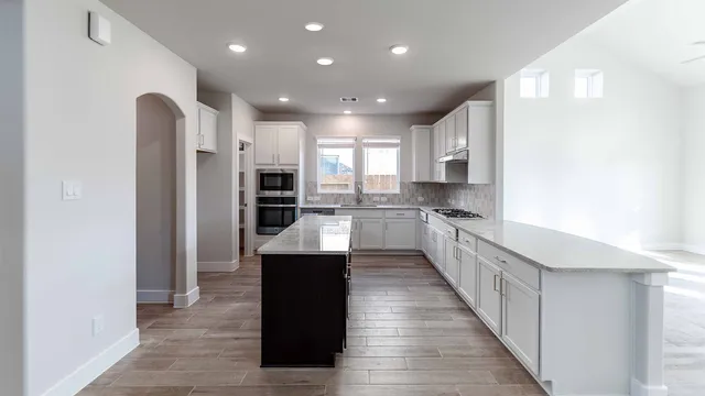 a large kitchen with stainless steel appliances kitchen island granite countertop a refrigerator and a sink