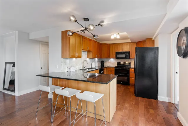 a kitchen with stainless steel appliances granite countertop a refrigerator a sink dishwasher a stove and a dining table with wooden floor