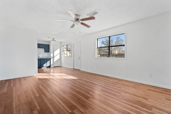an empty room with wooden floor chandelier fan and windows