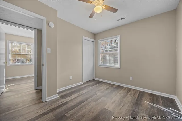 an empty room with wooden floor fan and windows