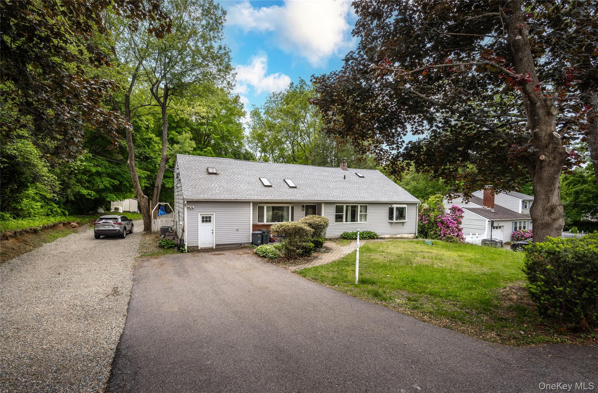 View of front of property featuring asphalt driveway, a front yard, a shingled roof, and view of wooded area
