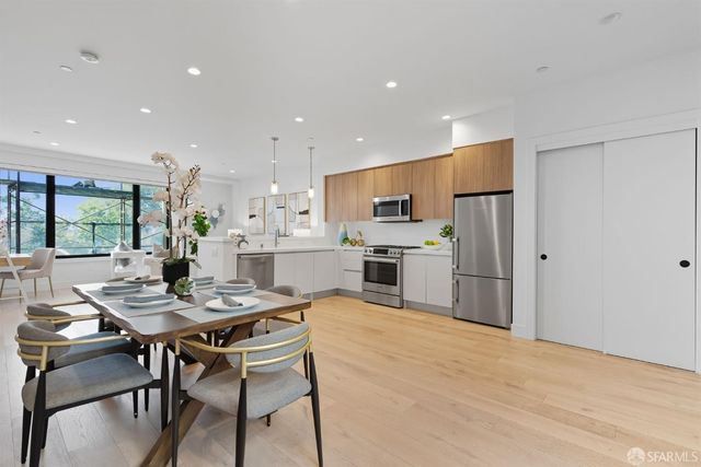 a kitchen with stainless steel appliances kitchen island granite countertop a dining table chairs refrigerator and cabinets