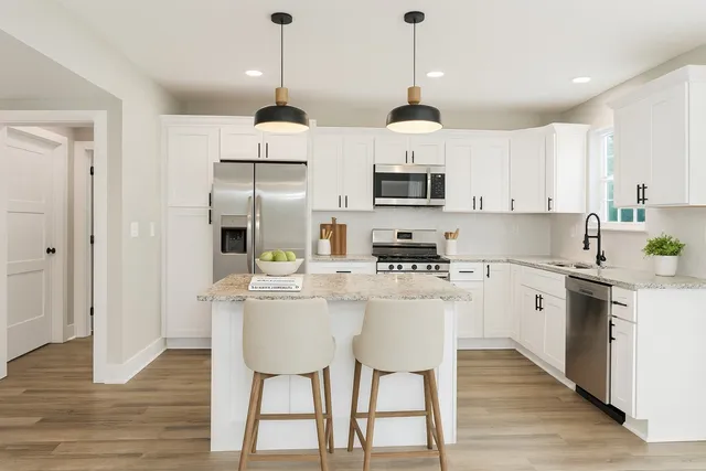 a kitchen with stainless steel appliances a stove a sink a refrigerator and white cabinets with wooden floor