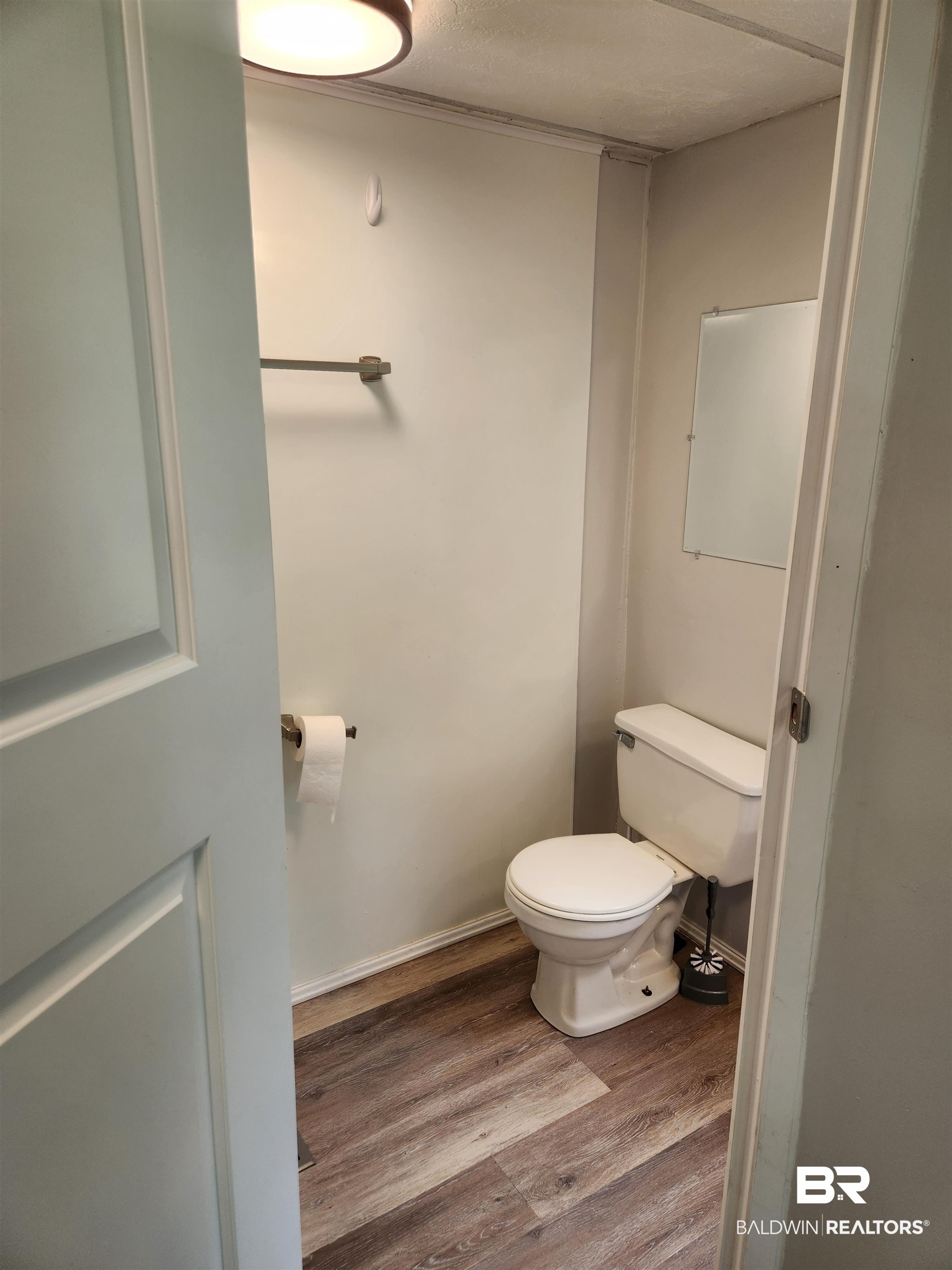23051 Fritz Lane Foley, AL 36535 - Photo 13 of 26 Powder room featuring wood-finish flooring, a contemporary ceiling light fixture, a wall-mounted mirror, and a white toilet