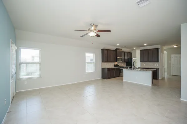 a view of an empty room and kitchen with fireplace ceiling fan