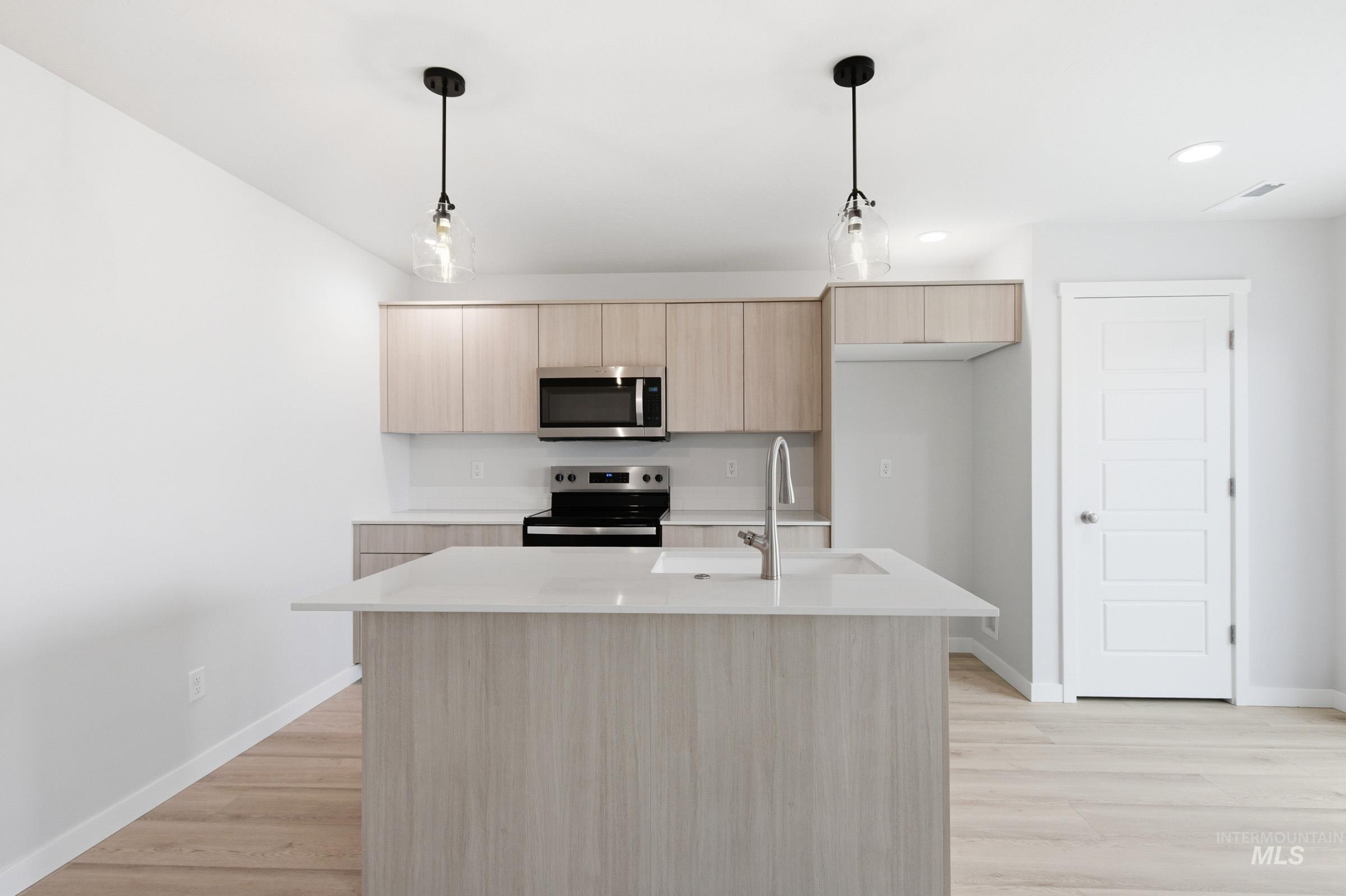 10784 Rutland Street Caldwell, ID 83605 - Photo 4 of 21 Kitchen featuring light wood finish cabinetry, hanging light fixtures, an island with sink, and stainless steel appliances