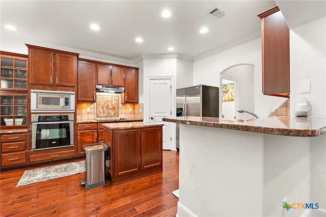 a kitchen with stainless steel appliances granite countertop wooden cabinets a stove a sink and dishwasher a refrigerator with wooden floor