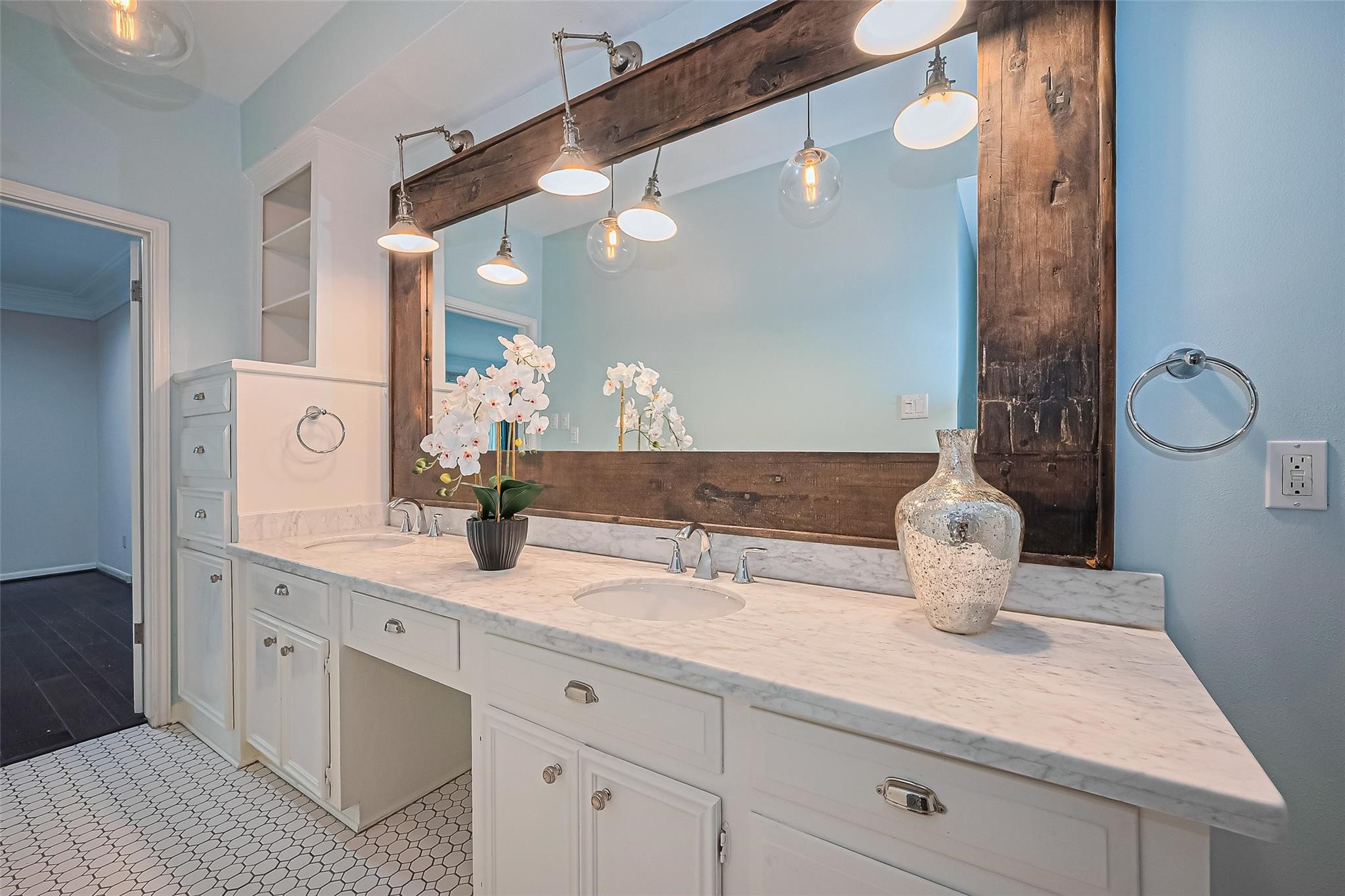 4305 Westheimer Road Houston, TX 77027 - Photo 13 of 25 Stylish bathroom featuring a large, rustic framed mirror, elegant marble countertop, and ample storage with white cabinetry.