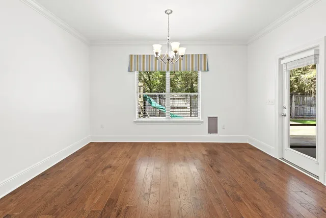 an empty room with wooden floor chandelier and windows