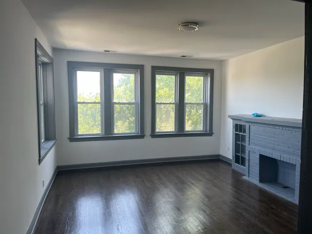 an empty room with wooden floor fireplace and windows