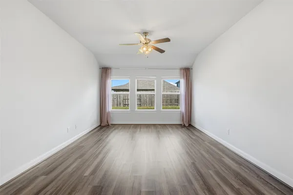 an empty room with wooden floor chandelier fan and windows