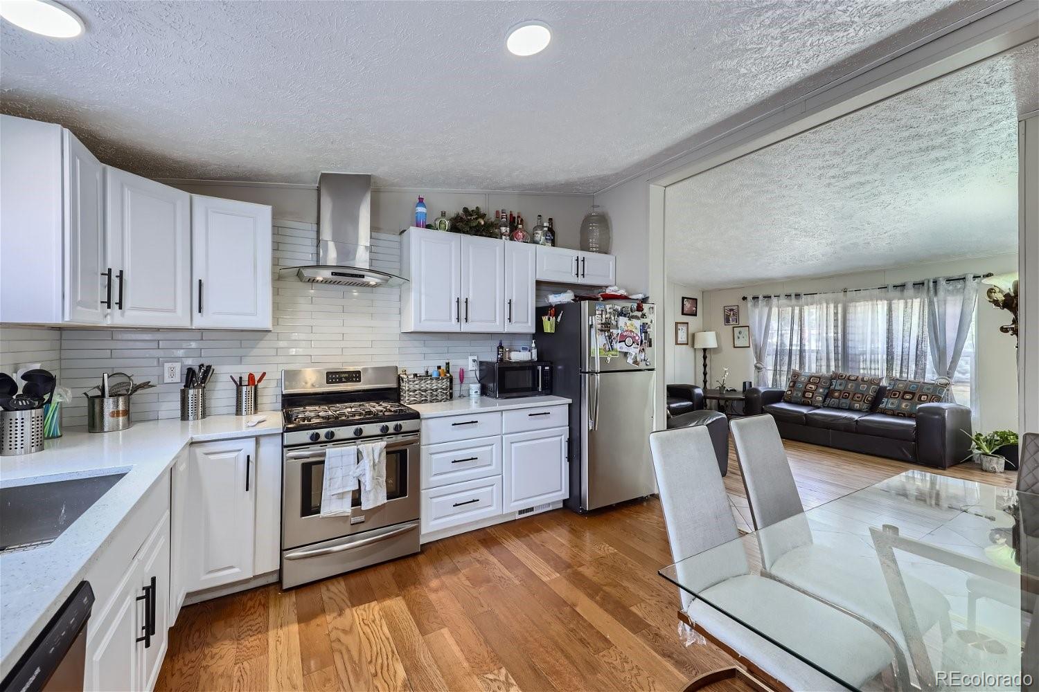 11682 Frederick Street Fort Lupton, CO 80621 - Photo 4 of 11 a kitchen with granite countertop a stove top oven a sink dishwasher and white cabinets with wooden floor