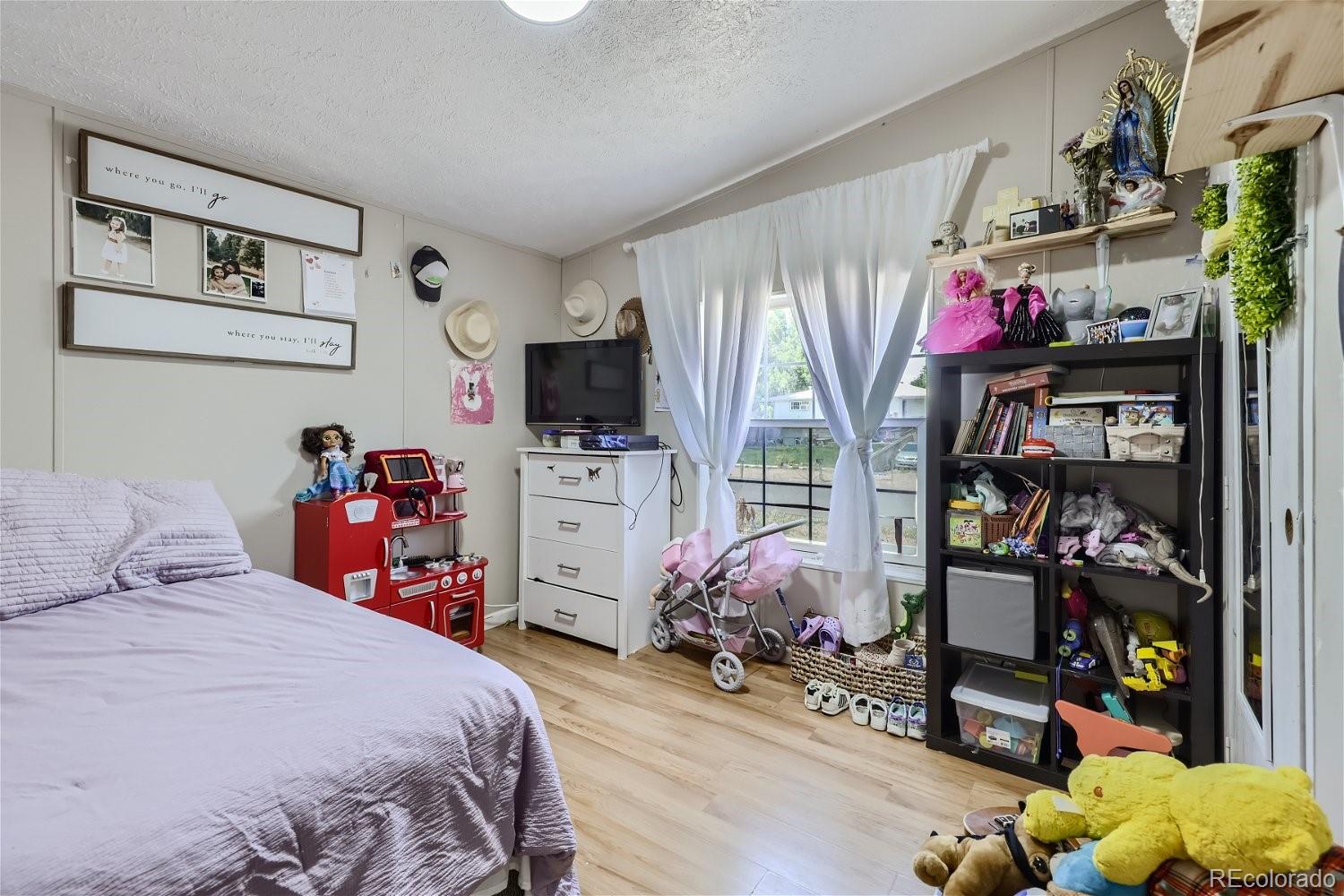11682 Frederick Street Fort Lupton, CO 80621 - Photo 7 of 11 a bedroom with a bed a flat screen tv and dresser