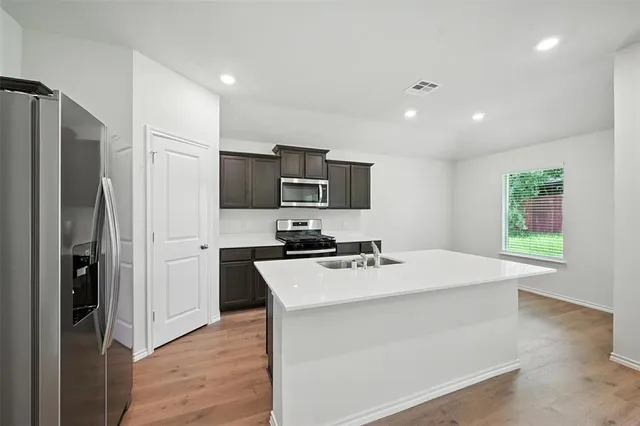 a kitchen with stainless steel appliances a sink a stove a refrigerator cabinets and wooden floor