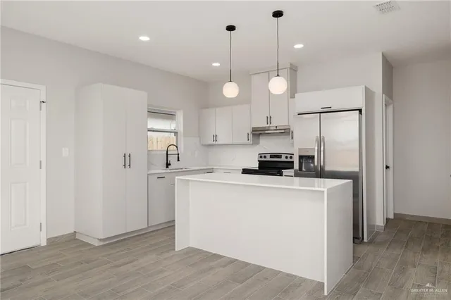 a kitchen with stainless steel appliances a stove a sink a refrigerator a center island and cabinets