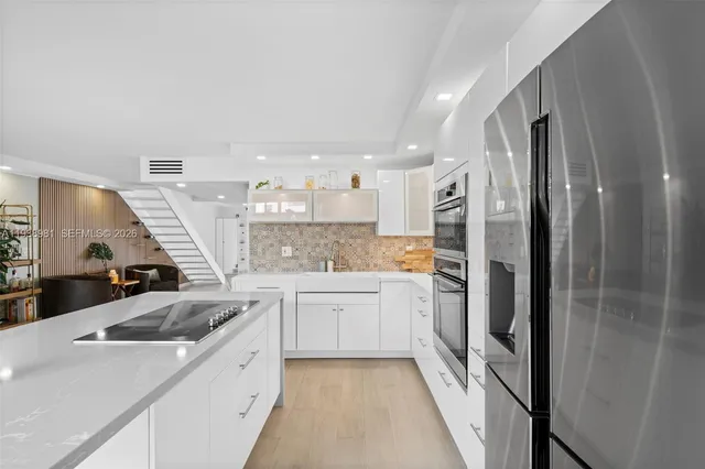 a kitchen with a sink dishwasher a refrigerator and white cabinets with wooden floor