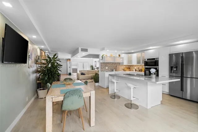 a living room with stainless steel appliances furniture a flat screen tv and a kitchen view