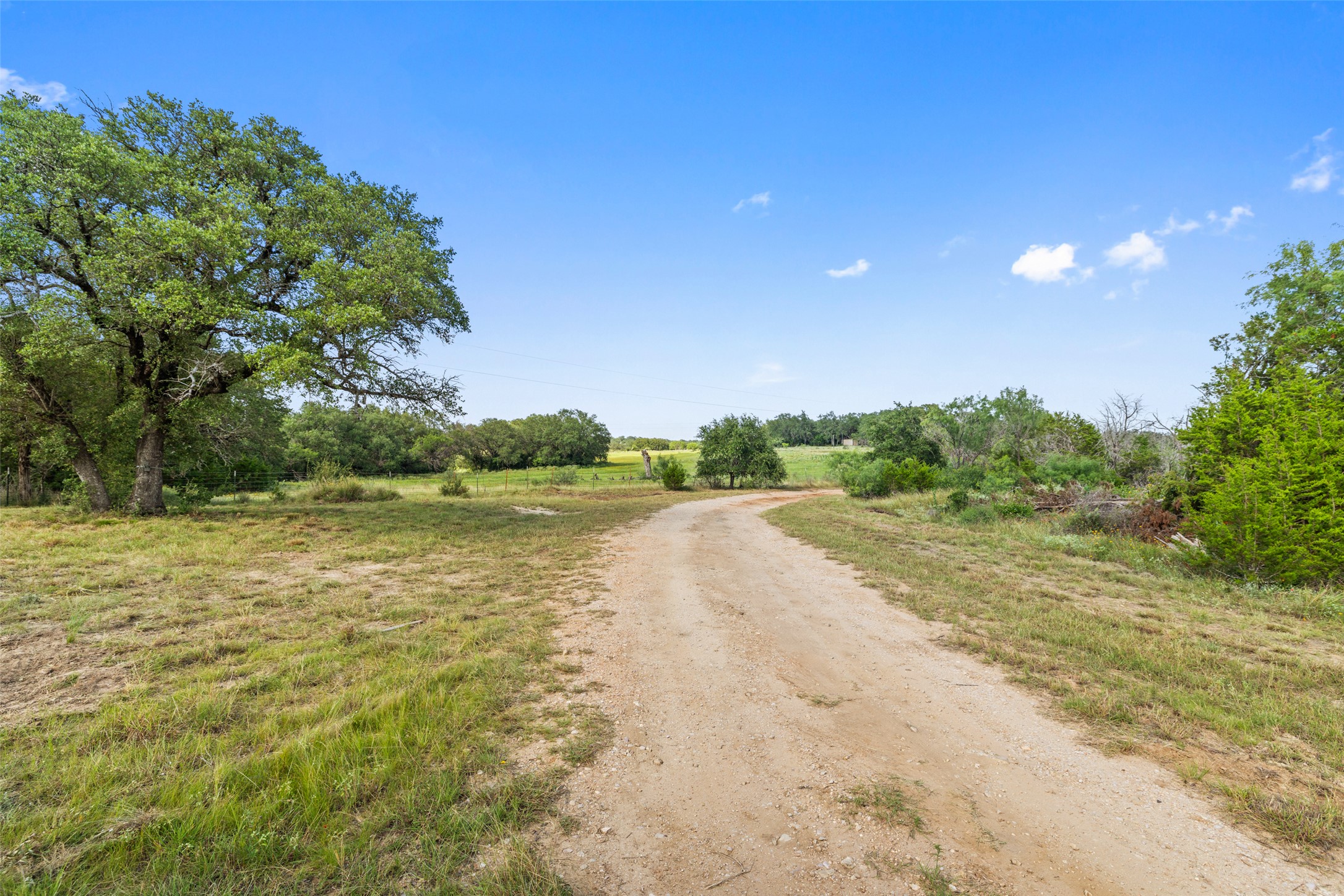764 Stubbs Road Johnson City, TX 78636 - Photo 25 of 29 A sweeping gravel driveway meanders through a generous lot, framed by mature trees and verdant acreage.