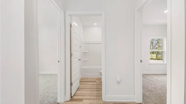 a view of a hallway with wooden floor and a bathroom