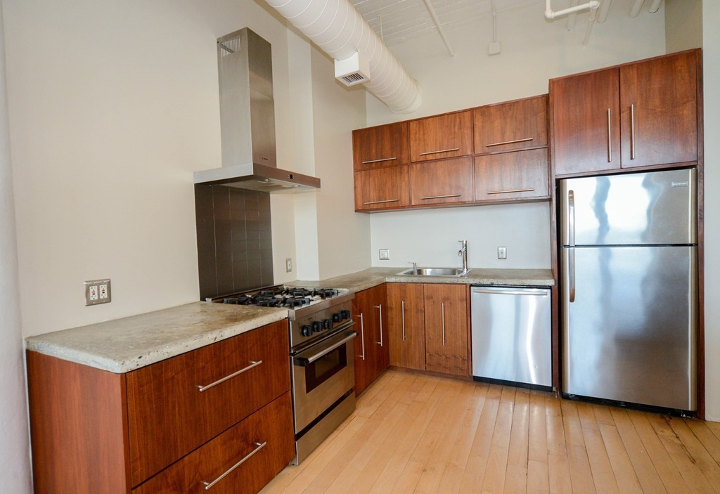 437 D Street, Unit 2C Boston, MA 02210 - Photo 4 of 13 a kitchen with stainless steel appliances granite countertop a stove a refrigerator and a sink with wooden cabinets
