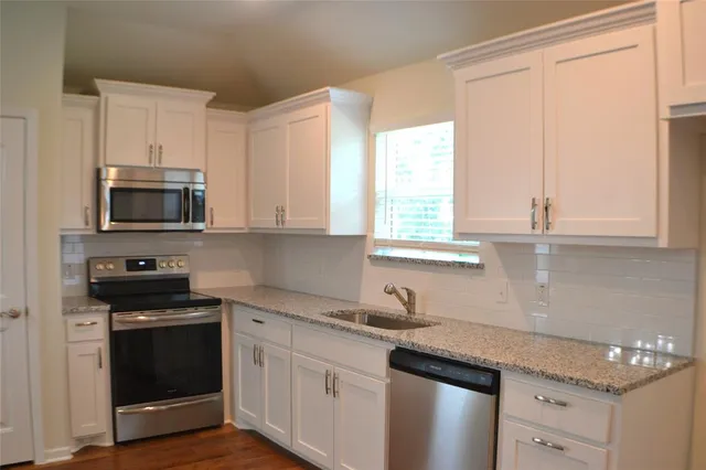 a kitchen with stainless steel appliances granite countertop white cabinets sink and a window