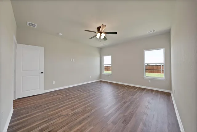 an empty room with wooden floor ceiling fan and windows