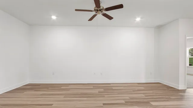 a view of an empty room with wooden floor and a ceiling fan