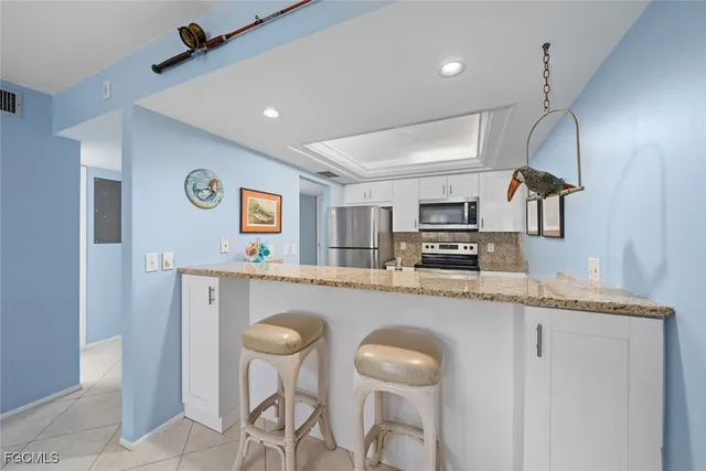 a kitchen with stainless steel appliances granite countertop a sink a stove a refrigerator a microwave oven with white cabinets and wooden floor