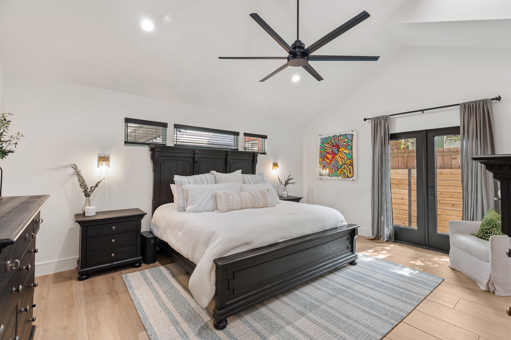 2626 Reagan Street Houston, TX 77009 - Photo 18 of 50 The rare downstairs primary bedroom features vaulted ceilings with a modern ceiling fan, gold wall sconces on each side of the bed, and French doors are open directly to the backyard, allowing for plenty of natural light.