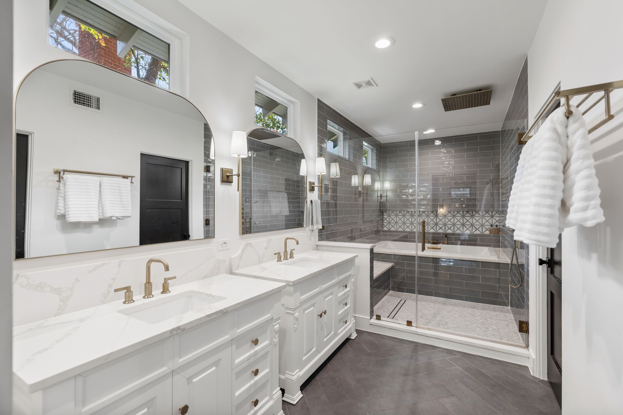 2626 Reagan Street Houston, TX 77009 - Photo 20 of 50 The spa inspired primary bathroom features dual vanities with marble countertops,gold fixtures throughout, gold framed mirrors with an elegant arched design, and gold wall sconces that add warmth and sophistication to the space. Large windows above the mirrors allow natural light to pour in, highlighting the custom cabinetry, ample storage, and thoughtfully designed layout that offers both style and everyday functionality.