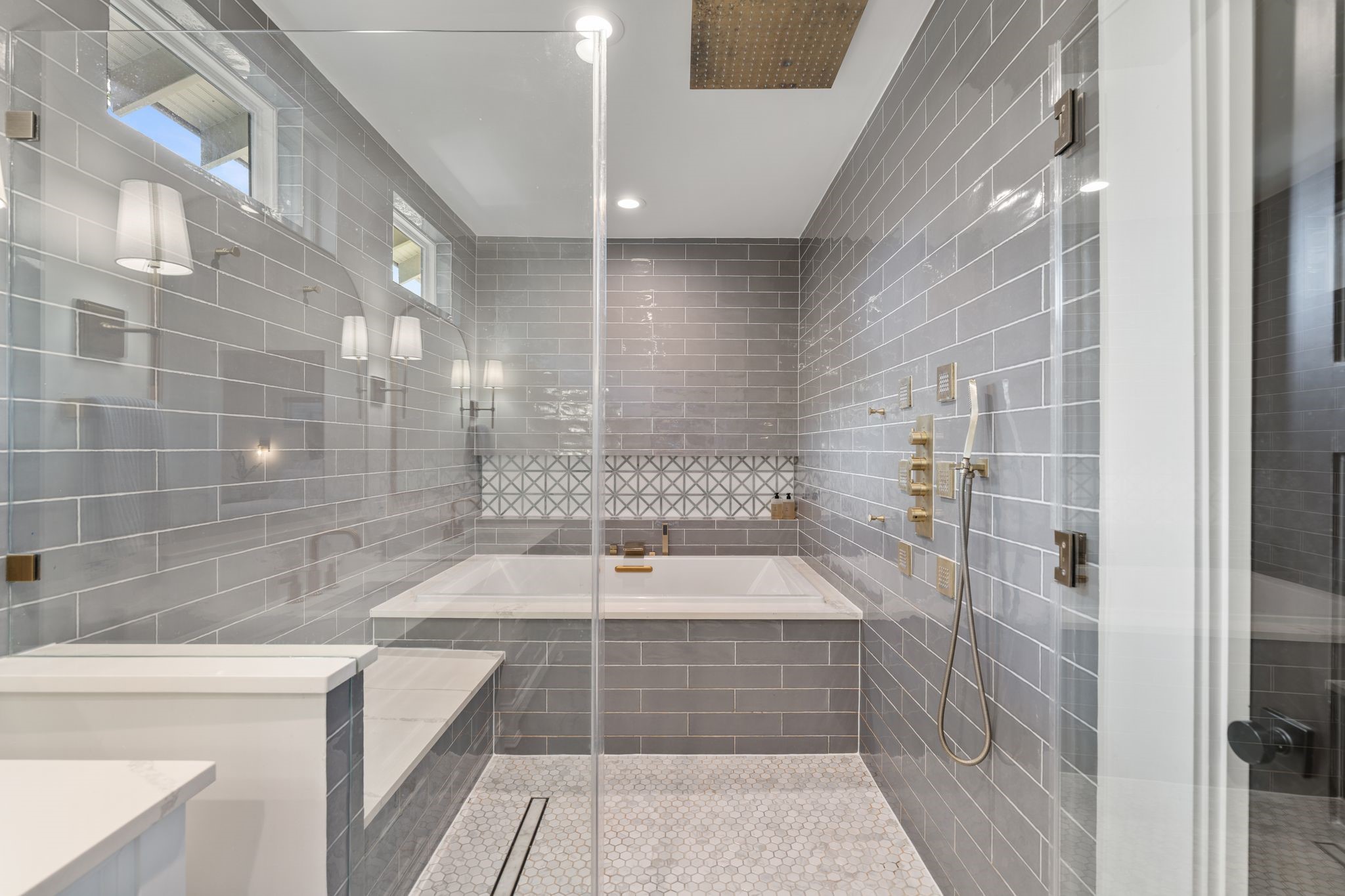2626 Reagan Street Houston, TX 77009 - Photo 21 of 50 The oversized walk-in shower with large rain shower head and 6 body sprayers showcases floor to ceiling gray tile with a herringbone accent design and a frameless glass enclosure, creating a striking focal point within the bathroom. Inside the shower, an oversized soaking tub offers a true spa-like experience.