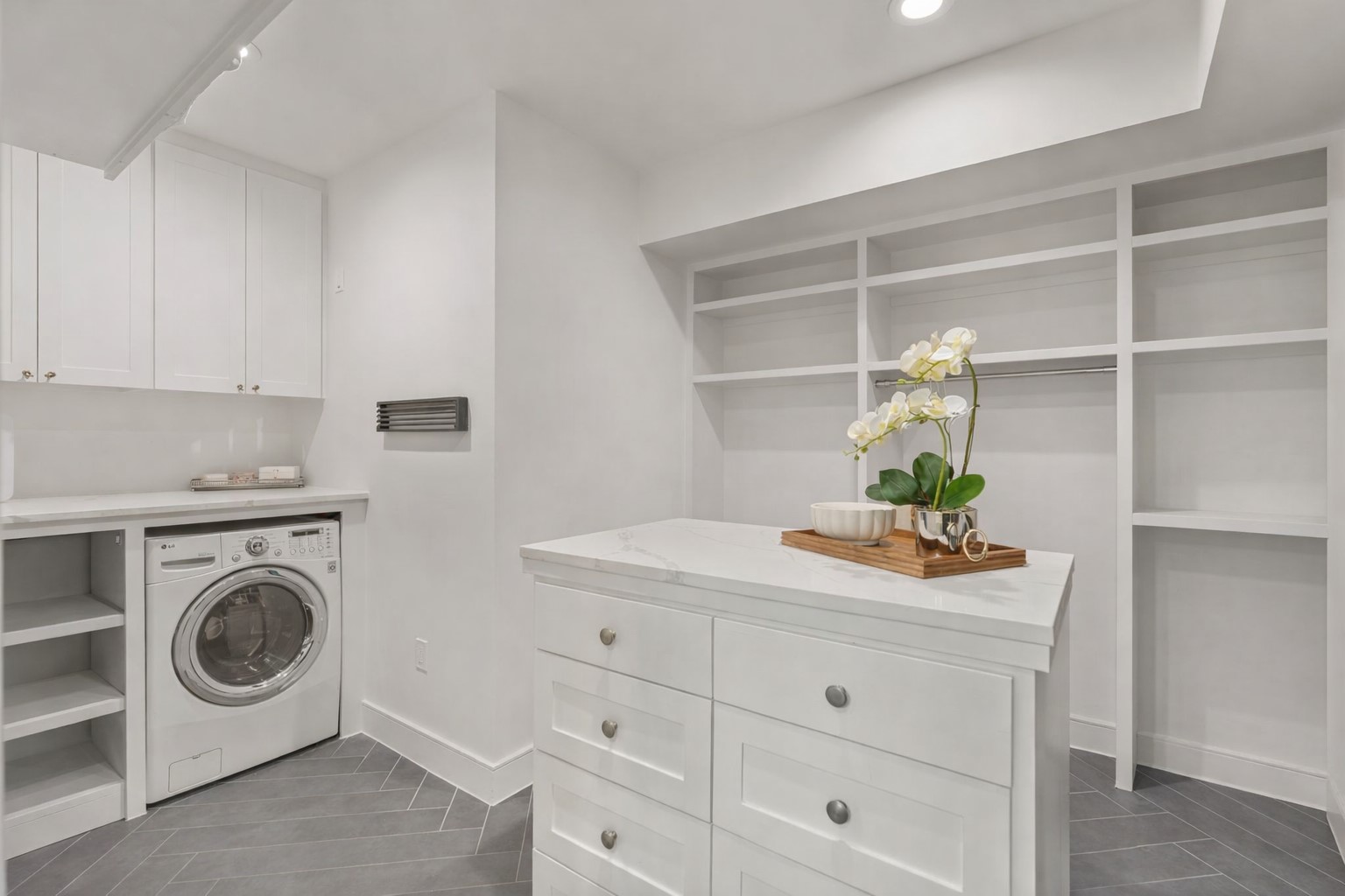 2626 Reagan Street Houston, TX 77009 - Photo 22 of 50 This custom designed primary closet features built-in shelving, hanging storage, and a center island with drawers for added organization. A dedicated laundry area with a washer/dryer combo, upper cabinetry, and a countertop provides a convenient space for folding, while the herringbone tile flooring adds a stylish finishing touch to this highly functional space. Note there is another large utility room upstairs.