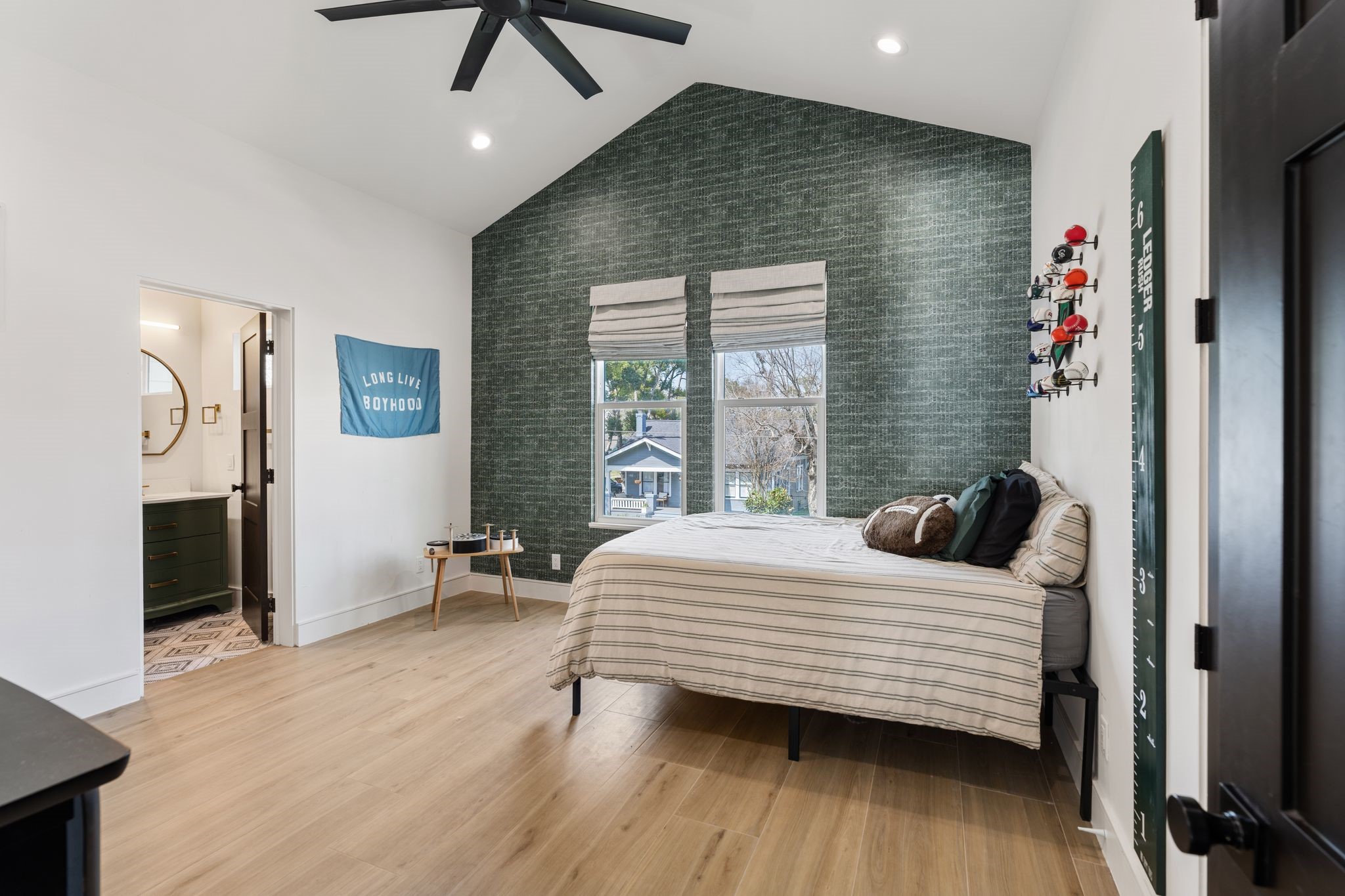 2626 Reagan Street Houston, TX 77009 - Photo 24 of 50 Secondary bedroom #1 features a vaulted ceiling, recessed lighting, and a modern ceiling fan that enhance the open and airy feel of the space. An accent wallpaper wall adds character and texture, while large windows with custom blinds bring in natural light.