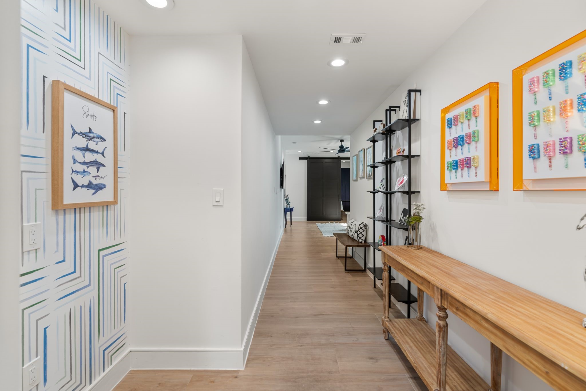 2626 Reagan Street Houston, TX 77009 - Photo 26 of 50 This upstairs hallway connects the flex space and the first bedroom to the additional bedrooms located at the front of the home. This long hallway features recessed lighting, warm wood flooring, and a decorative wallpaper that creates a perfect space for displaying artwork, photos, or kids' creations, adding personality and charm to the hallway.